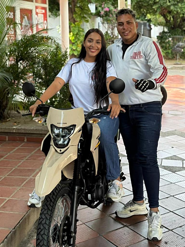 Mujer con camiseta blanca en una motocicleta, acompañada de un hombre a su lado.