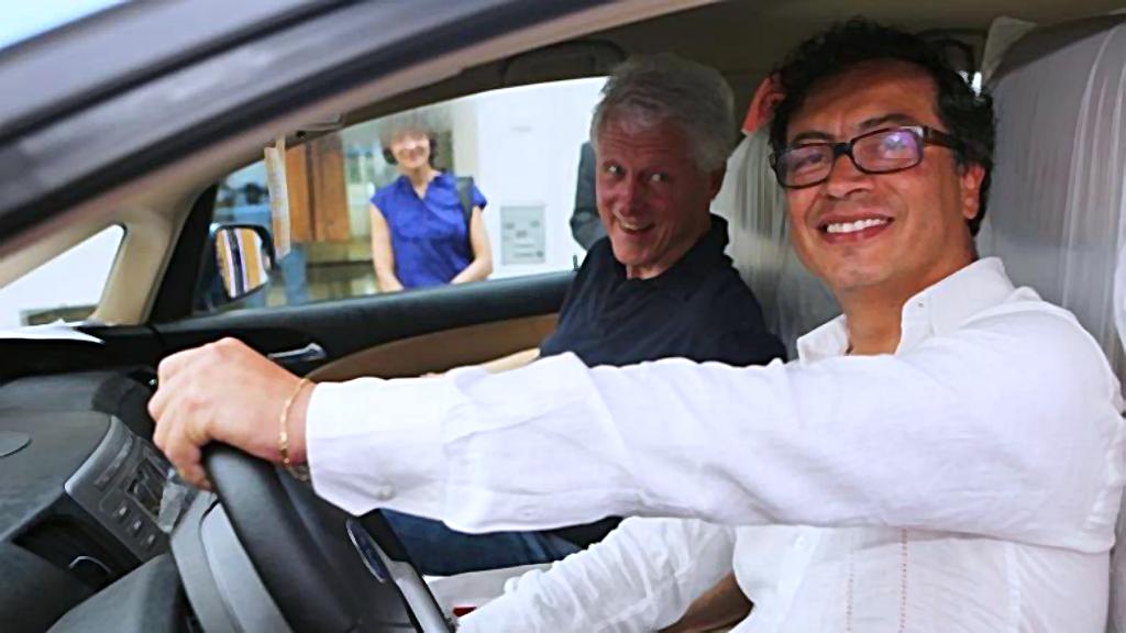 Primer plano de Gustavo Petro al volante de un automóvil, a su lado Bill Clinton como pasajero.
